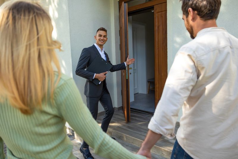 real estate agent guiding couple inside modern residence with open door in bright daylight