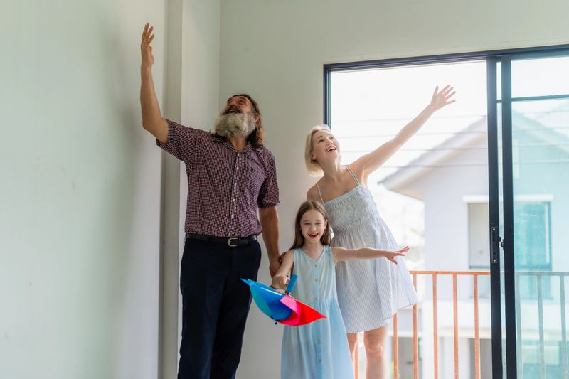 Excited family celebrating the purchase of their new dream home, looking around the empty room. Happy parents and daughter with a pinwheel, imagining the future in their new unfurnished house.