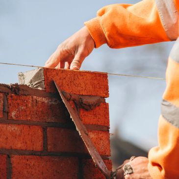 Bricklayer building a wall with red bricks and mortar.