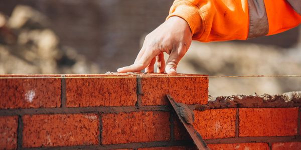 A worker laying bricks and smoothing mortar on a wall.