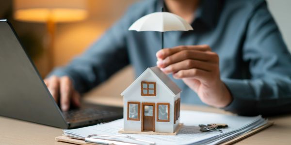 Person holding umbrella over a small house model on documents.
