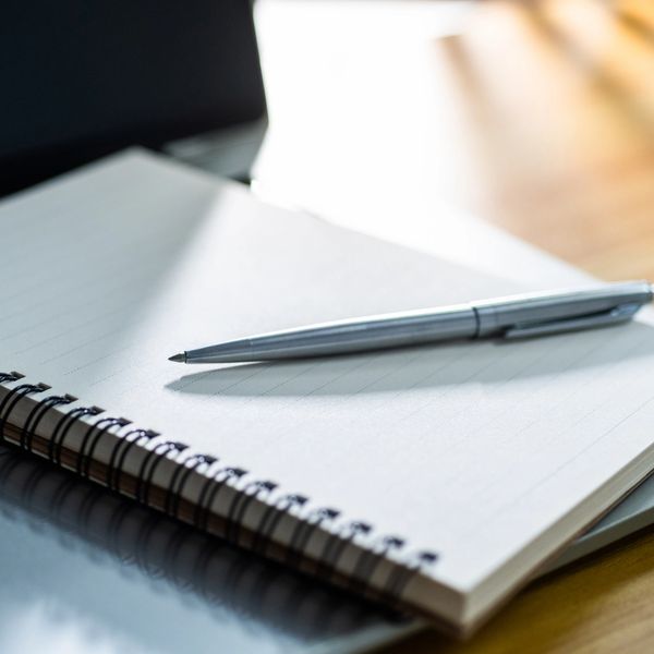 A silver pen resting on an open spiral notebook with lined pages.