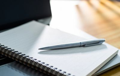 A silver pen resting on an open spiral notebook with blank pages.