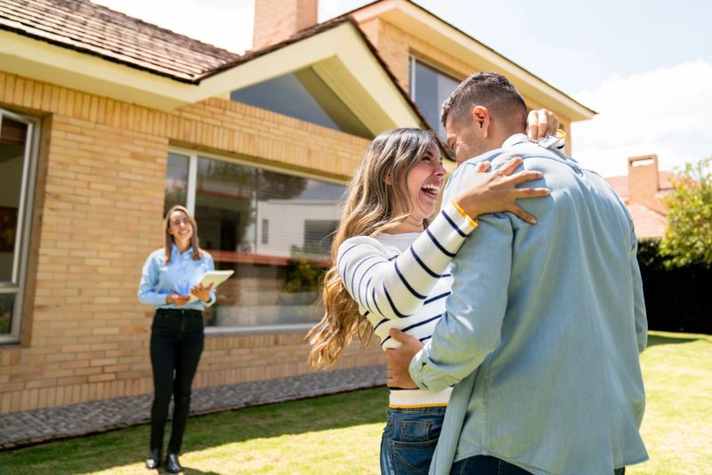 Happy couple buying a house and celebrating in front of the real estate agent after getting the keys - home ownership concepts