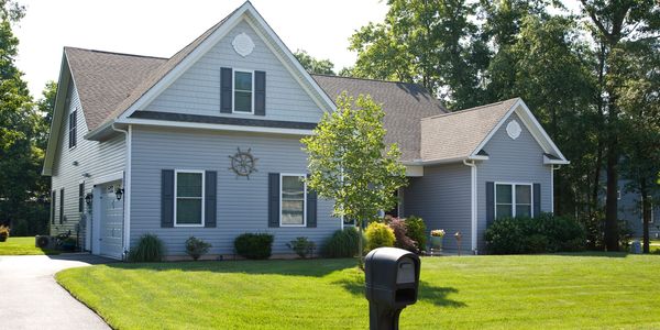 A gray suburban house with a well-maintained lawn and a black mailbox.