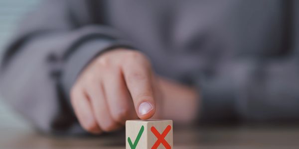 Finger pointing at a wooden block with check and cross marks.