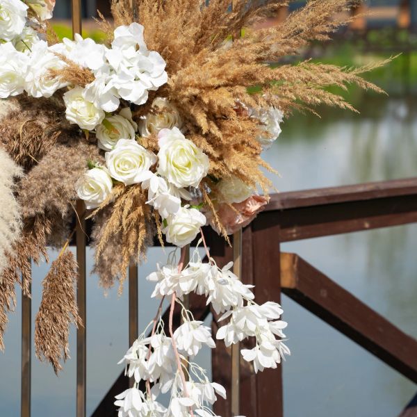 White flowers and dried grasses arranged on a wooden railing.