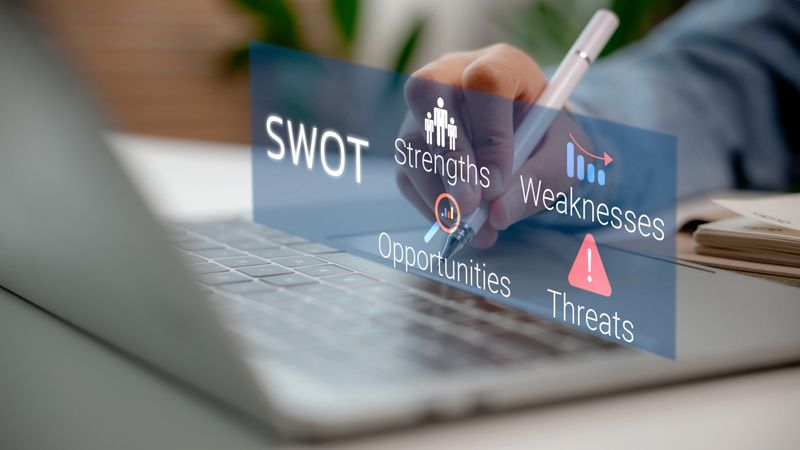 Hand holding pen pointing to virtual SWOT analysis on laptop, showing business strengths, weaknesses, opportunities, and threats, perfect for strategic planning and business concept.