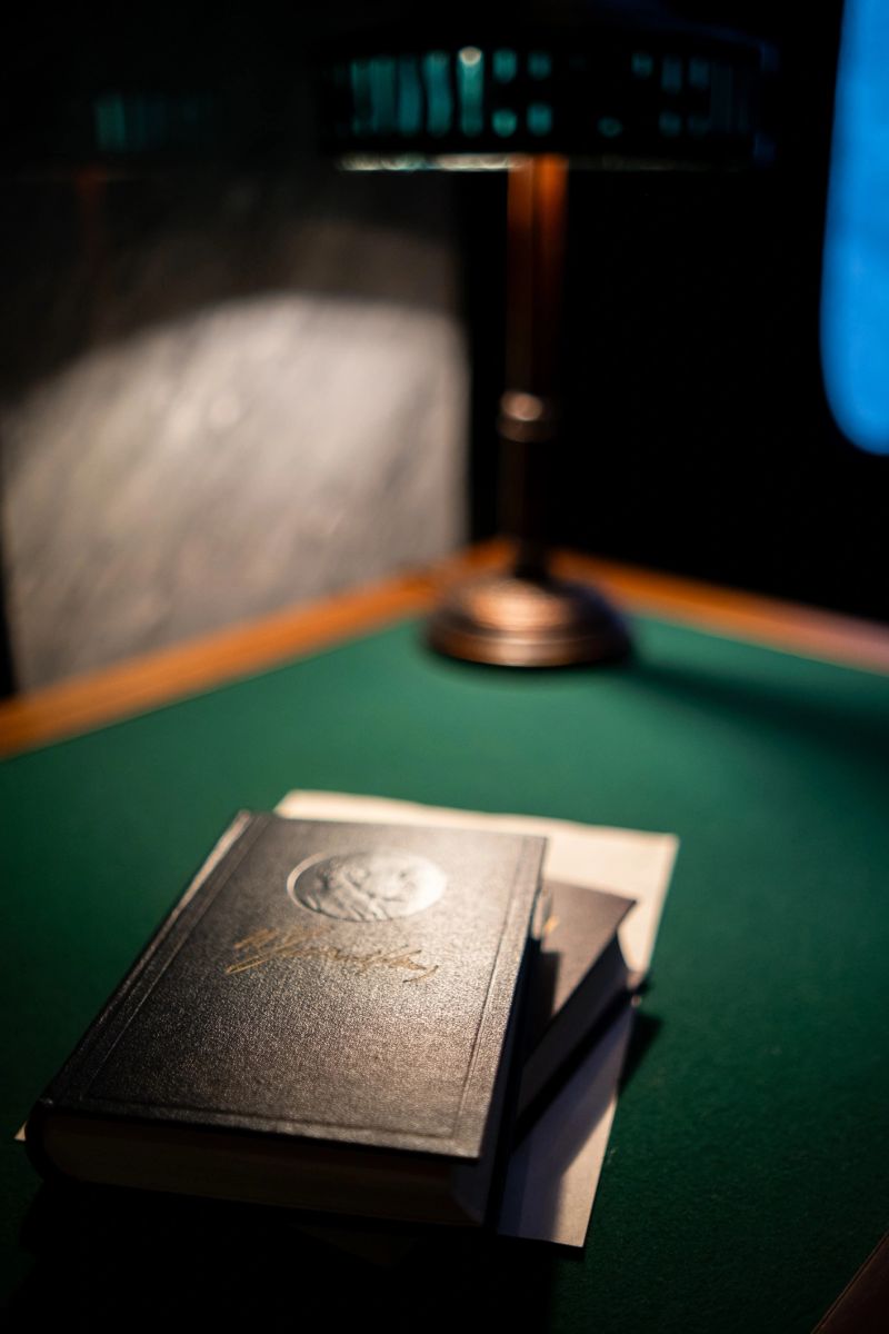 Leather-bound books sit atop a green felt table with a brass lamp glowing softly, creating a warm and inviting atmosphere in a quiet study.