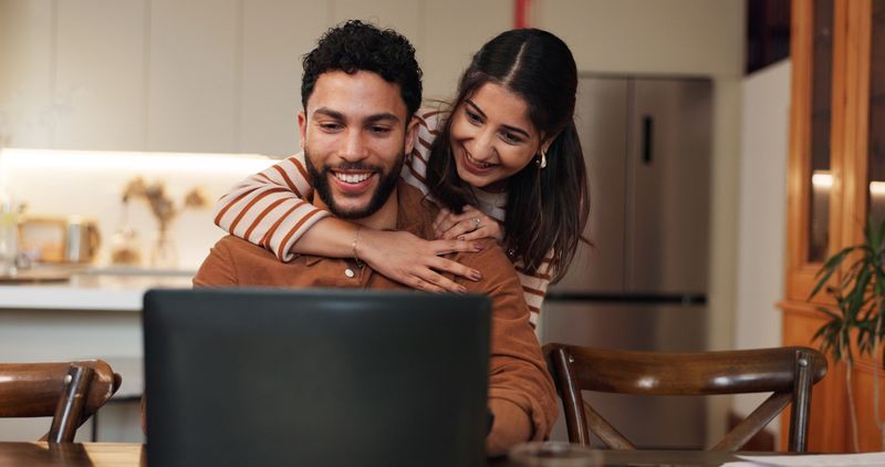 Couple, laptop and news of success in home, reading loan application response and support with win. Happy people, embrace husband and email announcement for mortgage insurance, celebrate and love
