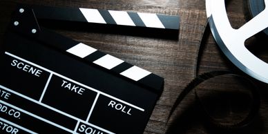 A film clapperboard and movie reel on a wooden surface.