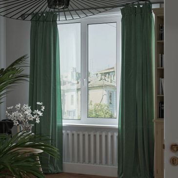 Window with green curtains and a vase of white flowers in a cozy room.