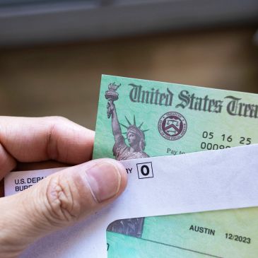 Hand holding a U.S. Treasury check partially pulled out of an envelope.