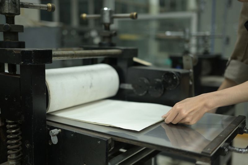 A close-up of an artist carefully placing dampened paper over an inked plate on an etching press, ensuring precise alignment before rolling it through for printmaking, Printmaking or Graphic art.