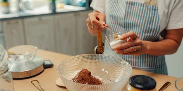Person scooping an ingredient into a glass while baking.