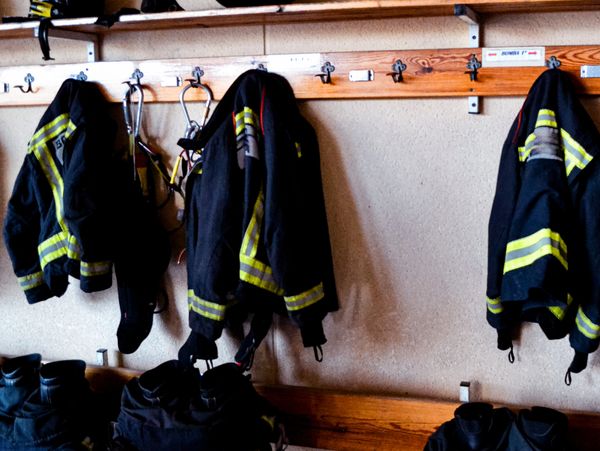 Firefighter gear including helmets, jackets, and boots hung neatly in a locker room.