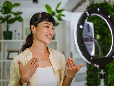 Woman recording a video using a ring light and phone.