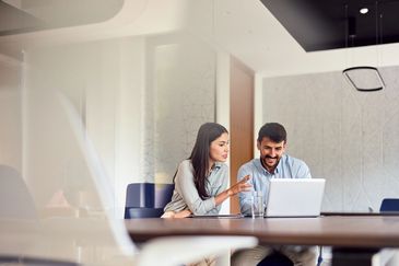 Two colleagues discussing work on a laptop in a modern office.