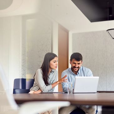 Two colleagues discussing work in an office while looking at a laptop.