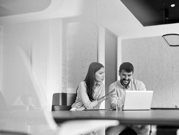 Two colleagues discussing work while looking at a laptop in a modern office.