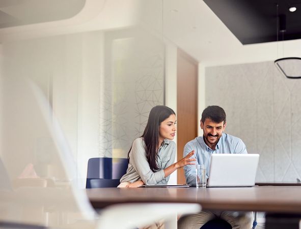 Two colleagues discussing work at a laptop in a modern office.