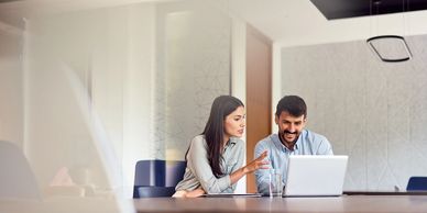 Two colleagues discussing work while looking at a laptop in a modern office.