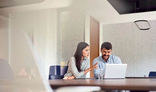 Two colleagues collaborating over a laptop in a modern office.