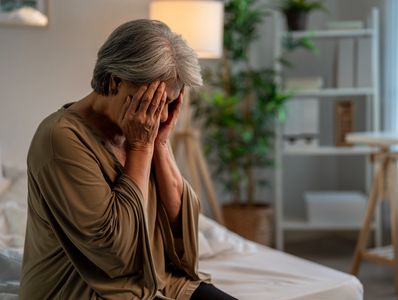 Elderly woman looking distressed, covering her face with her hands.