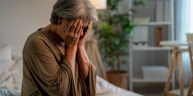 Elderly woman with hands on face, appearing stressed.