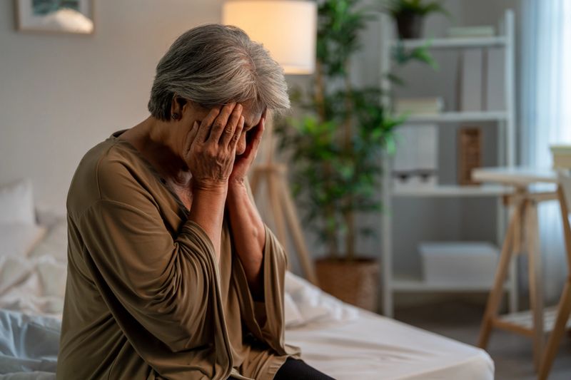 Asian senior elderly depressed woman sitting alone in bedroom at home. Attractive mature grandmother feeling sad, lonely and frustrated with life problem think of money debt, budget loss, bankruptcy.