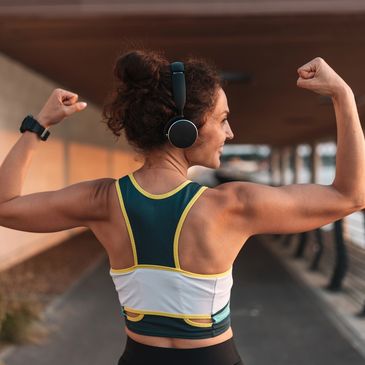 Woman in sportswear flexing muscles while wearing headphones outdoors.