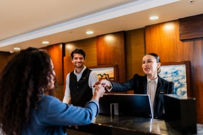 Hotel receptionist warmly greets a guest at the front desk.