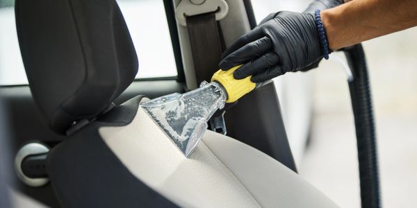 Cleaning car seat upholstery with a handheld extractor tool.