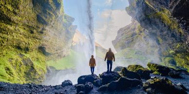 Two people standing inside a cave with a waterfall.