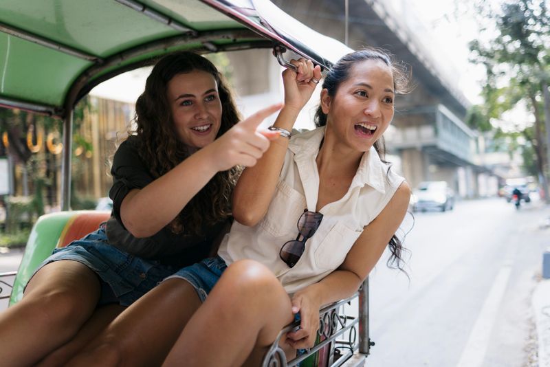 Two happy female tourists enjoying a ride on a tuk-tuk in bangkok, thailand, pointing out landmarks and soaking in the city's vibrant atmosphere