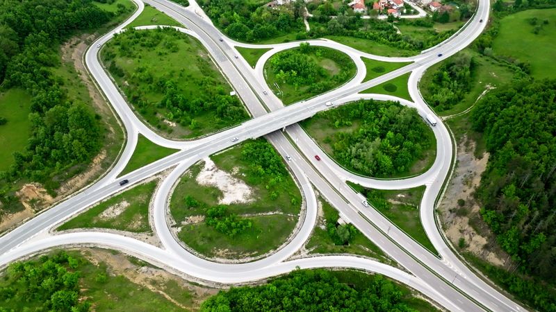 Transportation & carbon neutrality concept. Drone point of view directly above vehicles traveling on highway overpass amidst luxuriant green forest in spring.