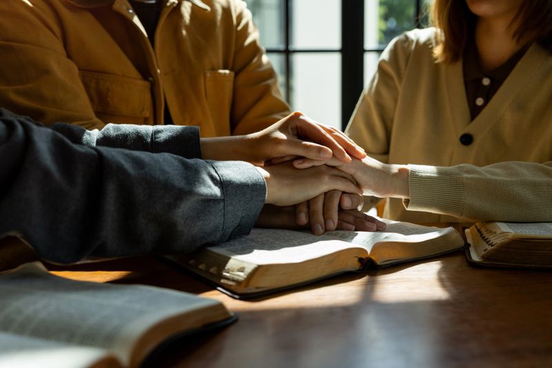 Christian group of people holding hands praying together over holy bible, comforting and praying together.