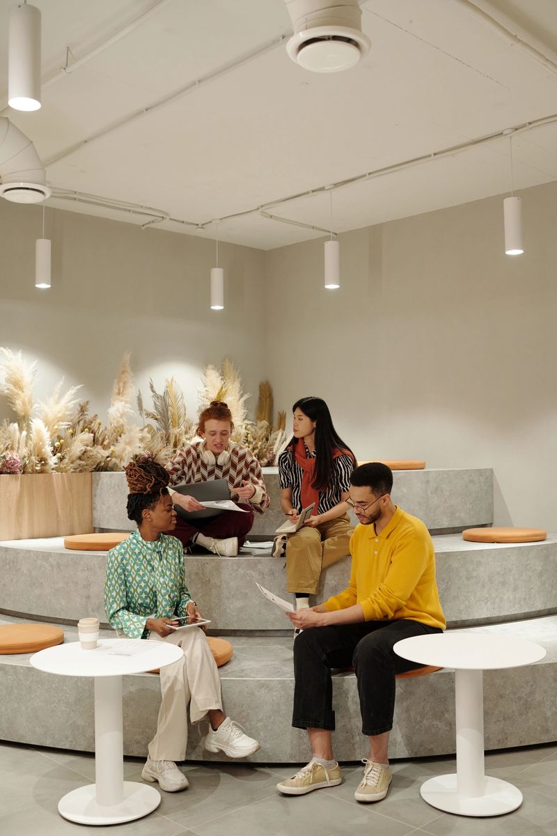 Group of young adult coworkers collaborating on creative project in modern coworking space, discussing documents, sitting on tiered seating
