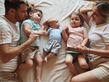 A family of five lying on a bed, holding hands and bonding.