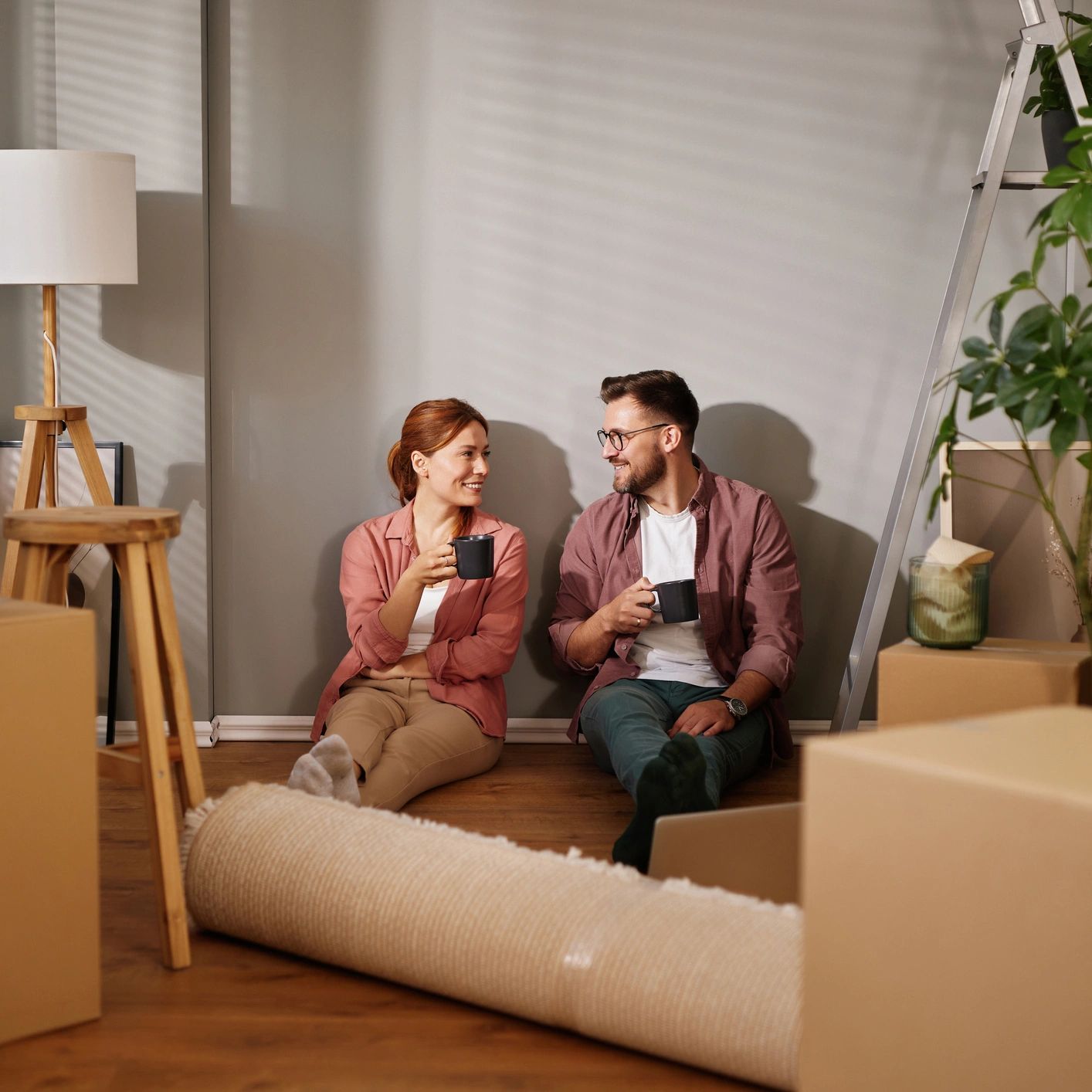 A smiling young couple taking a coffee break while moving into a new home. They are sitting on the h