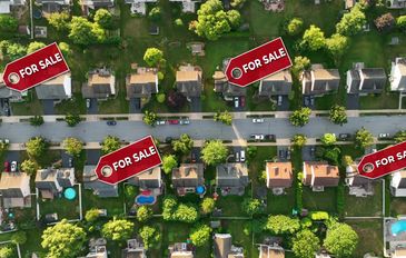 Aerial view of houses with 'For Sale' signs in a suburban neighborhood.