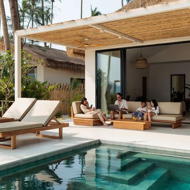 Family relaxing by the poolside on patio furniture at a modern tropical villa.