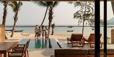 Family enjoying a beachfront view from a cozy patio with pool and wooden furniture.