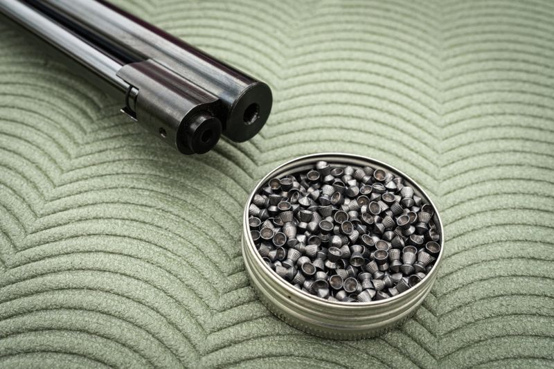 Close-up of an air rifle barrel and an open metal tin with pellets. Concept of sport shooting, hobby, and active recreation.