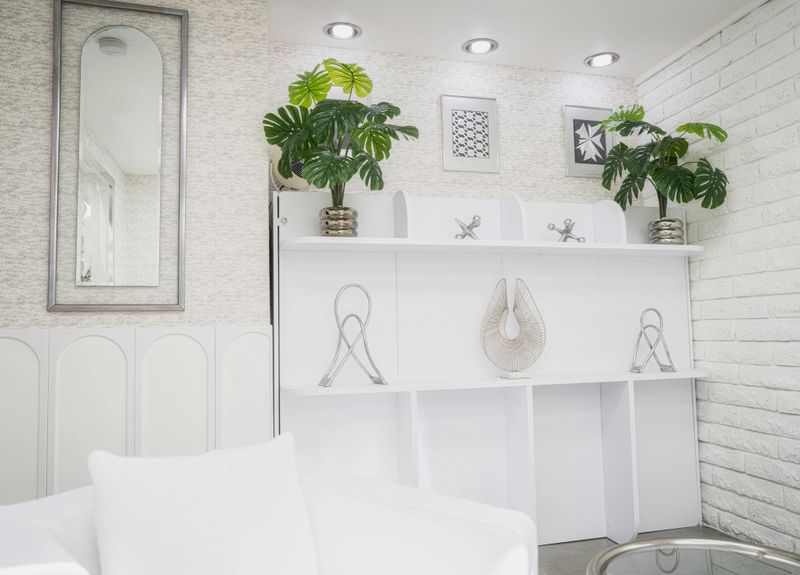 Stark white ultra-modern room with chrome art and green plants on a shelf, flanked by a vintage mirror and a white brick wall for a sleek curated look.