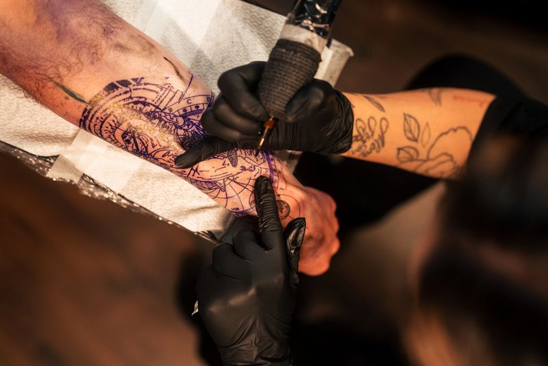 A close-up of a tattoo artist working on an arm, carefully inking an intricate pattern, with focus on technique and artistry, showcasing the tattooing process in a professional studio.