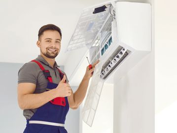 Technician giving thumbs up while repairing an air conditioner.