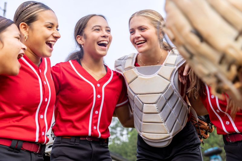 Softball girls laugh while discussing game in huddle on sidelines