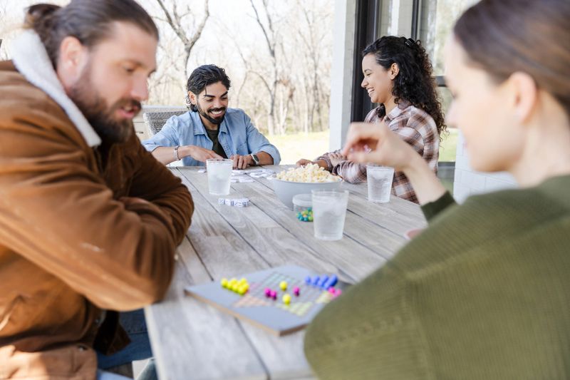 Multiracial group of friends enjoy a sunny day playing board games outdoors.
