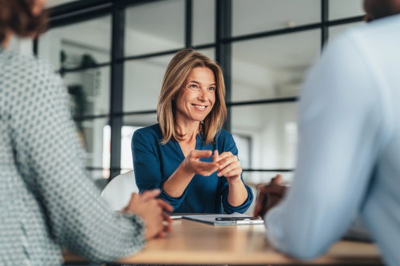 A candidate confidently presents their resume during a job interview with a panel of professionals.  Company owner on a meeting with employee. Middle aged businesswoman in a conversation with a colleague. Lawyer consulting client during formal meeting. Job interview and hiring process.